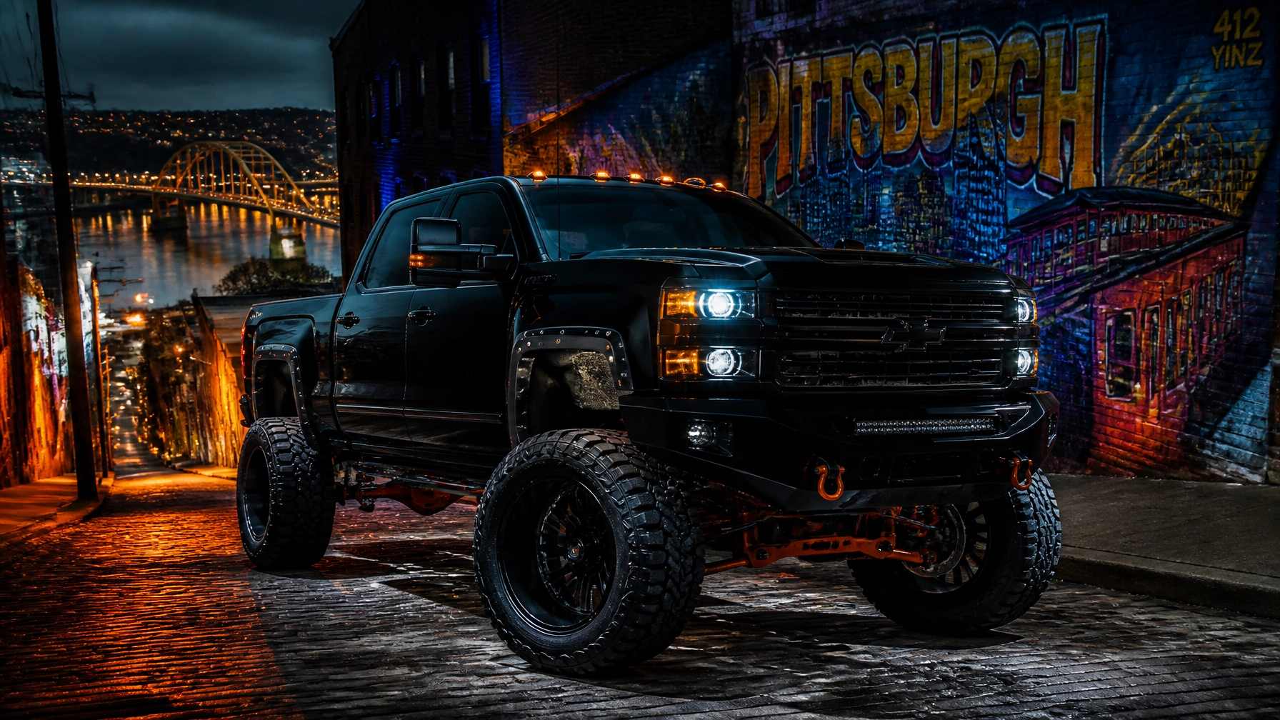 Black lifted pickup truck with bright headlights parked on a wet cobblestone street by a neon Pittsburgh mural at night.