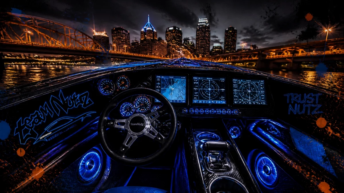 Nighttime view from a high-tech speedboat cockpit with blue-lit gauges and a city skyline in the distance.