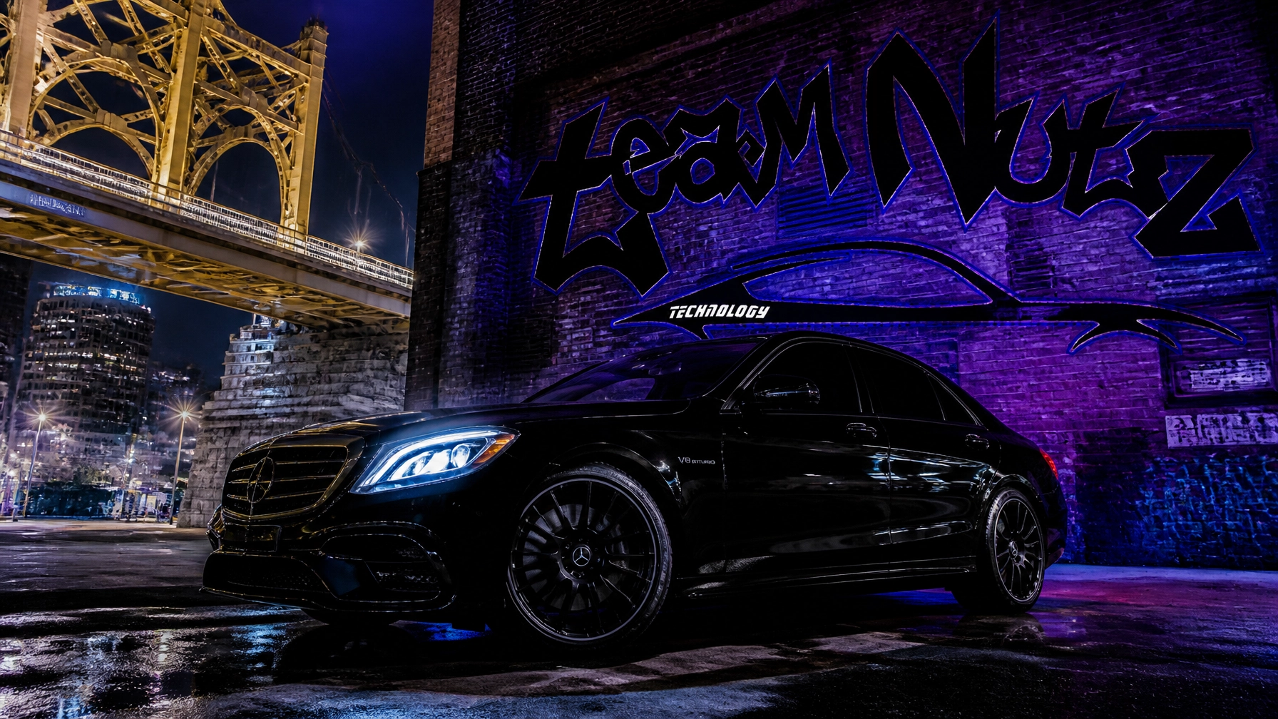 Black Mercedes-Benz sedan parked on a wet urban street at night, illuminated by purple-blue graffiti lighting beside a brick wall and a glowing yellow bridge in the background, reflections on the ground.