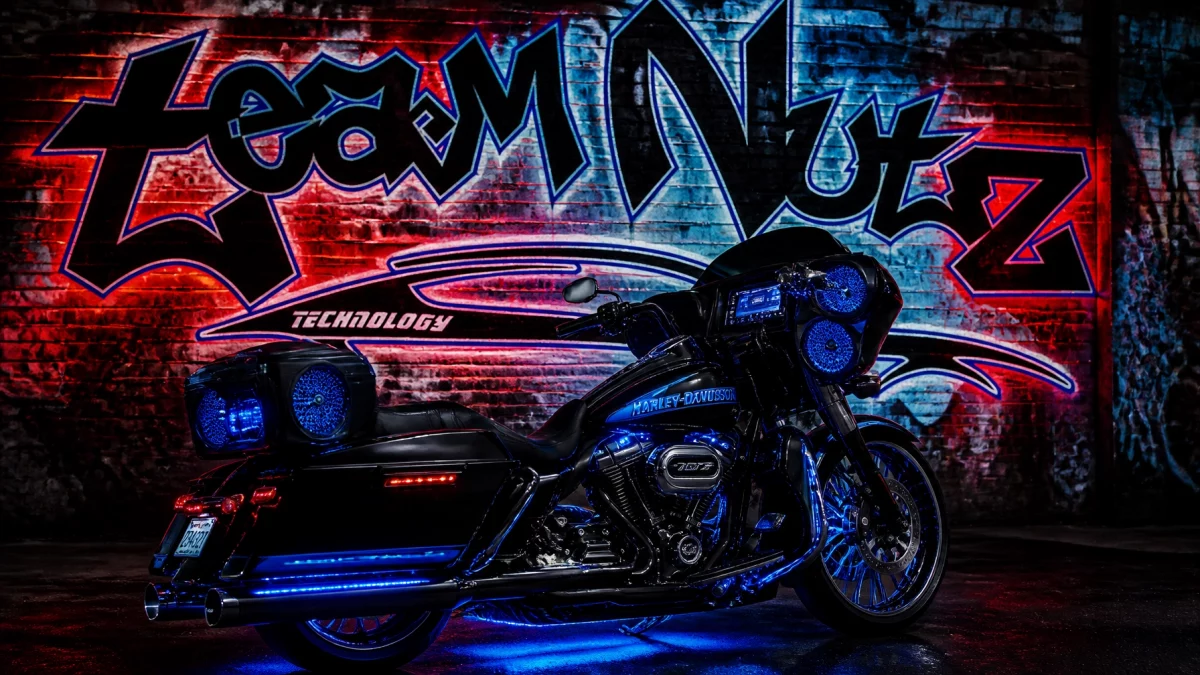 Black Harley‑Davidson touring bike with blue underglow lights parked in front of a neon graffiti wall.