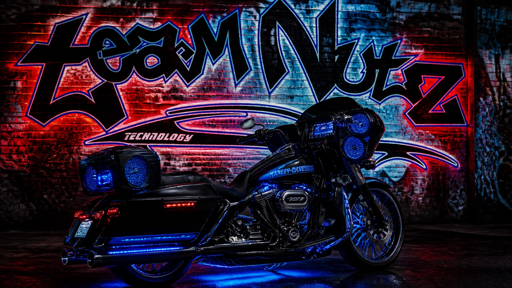 Black Harley‑Davidson touring bike with blue underglow lights parked in front of a neon graffiti wall.