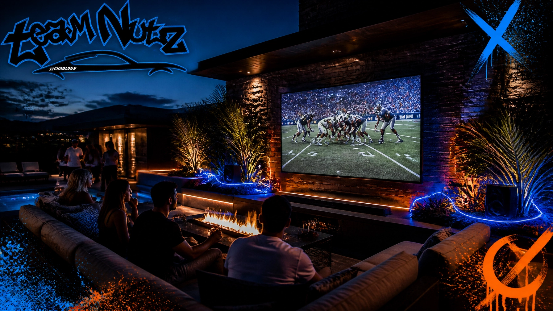 Group of people seated on a sofa watching a football game on a large outdoor screen at night, with blue and orange ambient lighting and a fire pit.