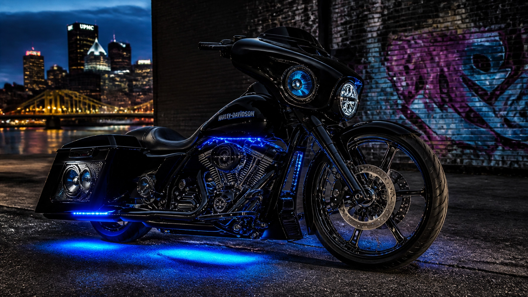 Black Harley‑Davidson motorcycle with blue underglow by a graffiti wall and city skyline at night, urban scene.