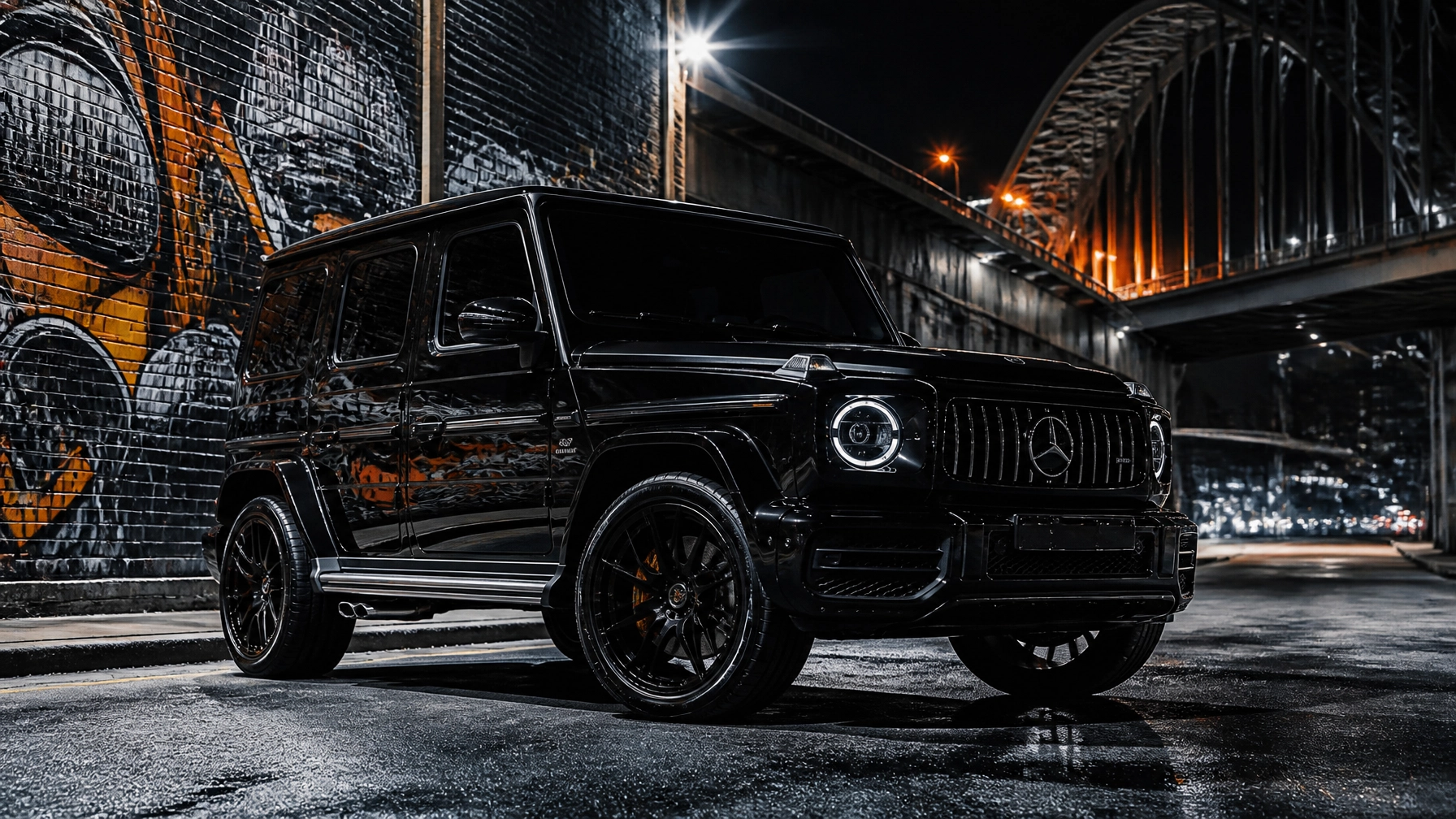 Black Mercedes-Benz G-Class SUV parked on a wet city street at night beside a graffiti-covered wall under an illuminated bridge.